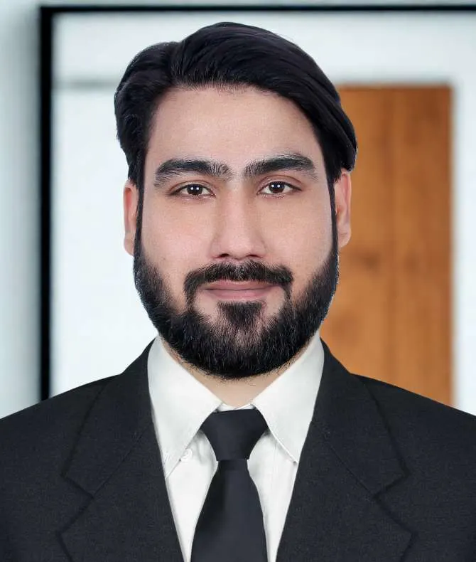 A man in a black suit and tie stands confidently against a neutral background, suggesting professionalism and formality.