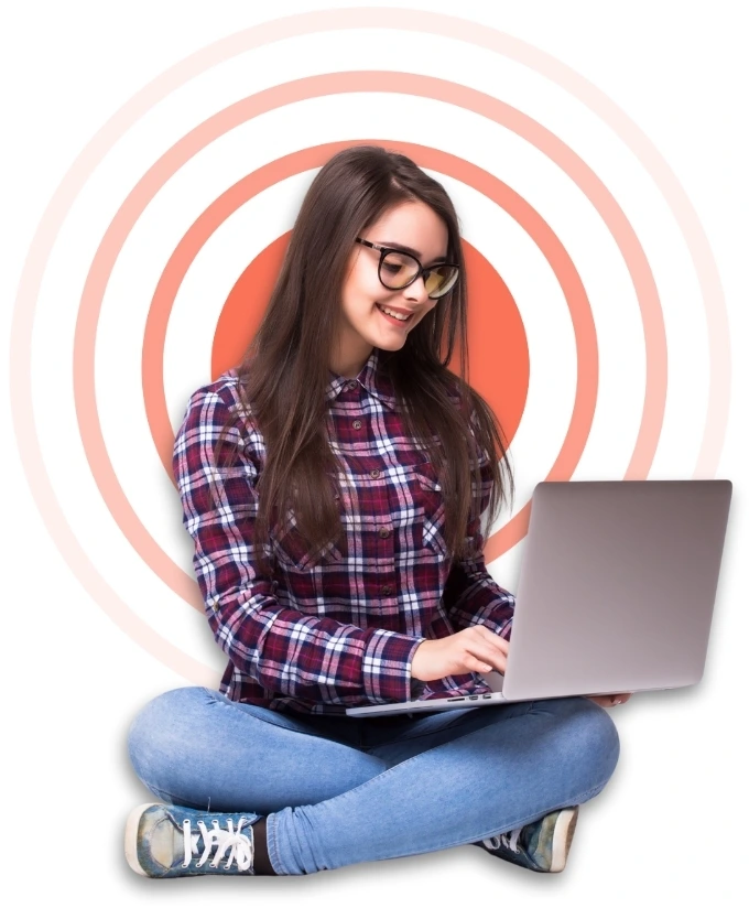 A woman with glasses sits cross-legged using a laptop against a patterned background.